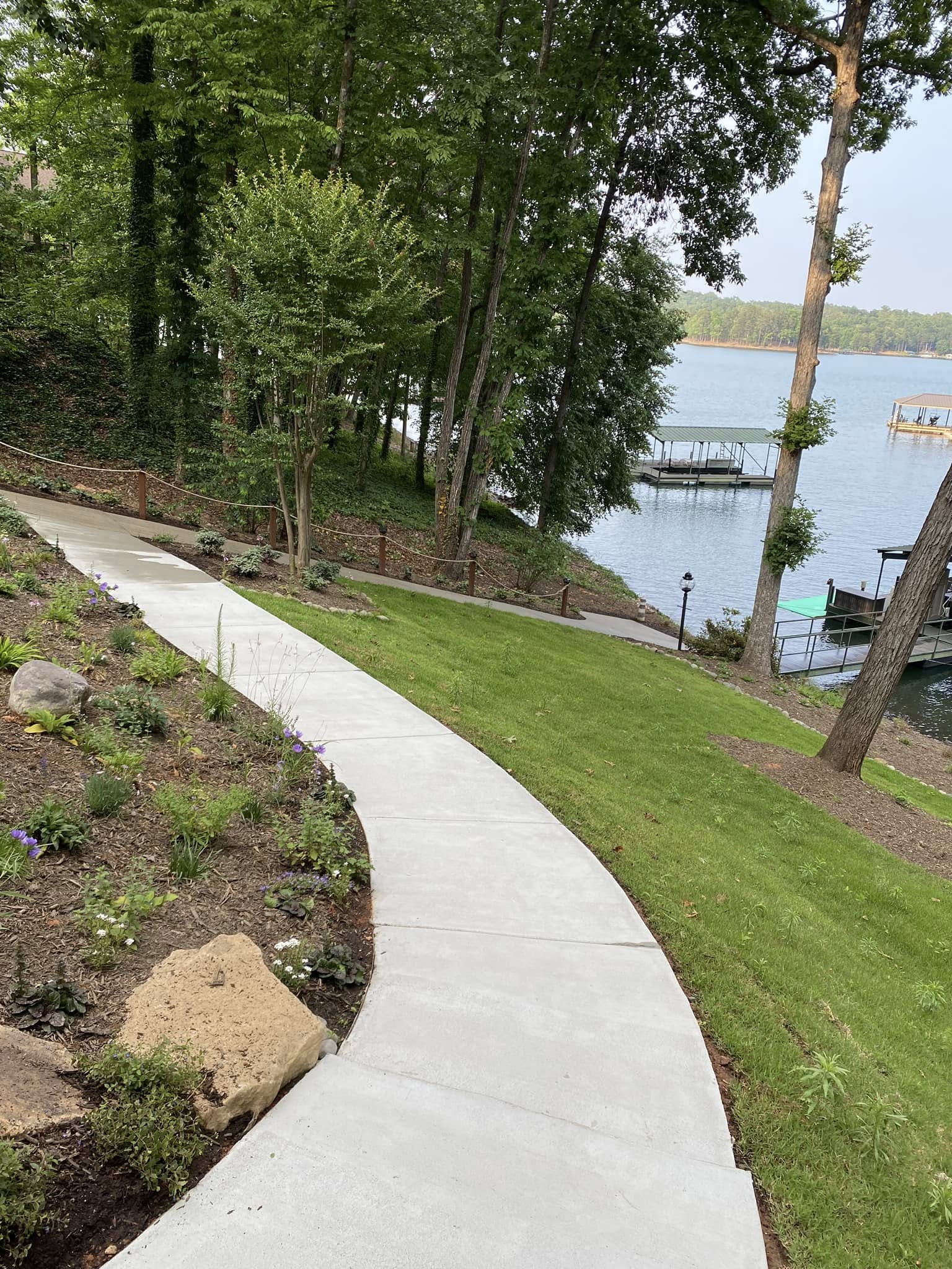 Clean light-gray concrete walkway curving down a landscaped hill toward a lake