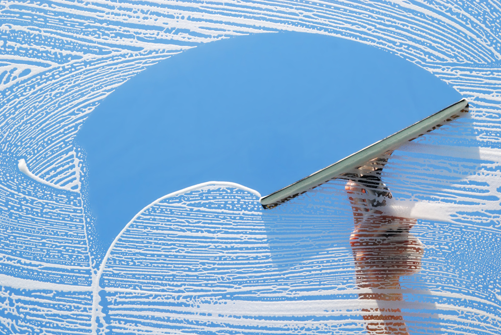 Hands using a squeegee on a soapy window